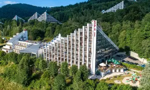 Hotel Diament Wisła w otoczeniu zieleni, z charakterystyczną architekturą schodkową i przeszklonymi fasadami.