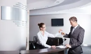 Miła technik hotelarstwa przekazuje klucze gościowi przy recepcji.