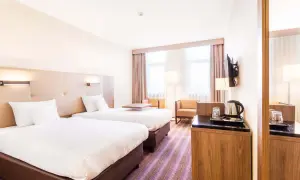 Pokój dwuosobowy w hotelu DeSilva Poznań z dwoma wygodnymi łóżkami, stolikiem i miejscem do przygotowania kawy.