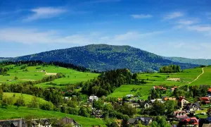 Zielone wzgórza i domy w Rabce Zdrój, z górami w tle.