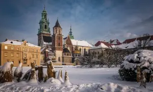 Zamek Królewski na Wawelu w zimowej scenerii. Pokryte śniegiem dachy i drzewa tworzą magiczny widok, idealny na kraków atrakcje zimą.