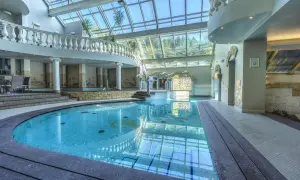 Basen w hotelu Szczyrk Klimczok z przeszklonym dachem, elegancką balustradą i mozaikami na ścianach.