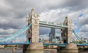 Słynny most w Wielkiej Brytanii, Tower Bridge, z charakterystycznymi wieżami i niebieskimi linami, na tle pochmurnego nieba.