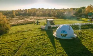 Nietypowe hotele: kopuła i piramida na tle jesiennego krajobrazu. Dym unosi się z ogniska obok kopuły.