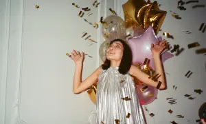 Kobieta w srebrnej sukience cieszy się deszczem złotych konfetti. W tle balony, idealnie na tematyczny sylwester.