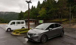 Szary Nissan i biały van na parkingu w Japonii. Widać, jaki ruch jest w Japonii, gdy podróżuje się po malowniczych terenach.