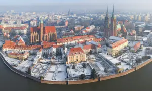 Wrocławskie atrakcje zimą: Ostrów Tumski pokryty śniegiem, z widokiem na katedrę i zabytkowe kamienice nad rzeką.