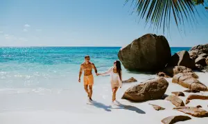 Para idealny czas na Seszele, kiedy jechać? Para spaceruje po rajskiej plaży z turkusową wodą i granitowymi skałami.