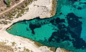 Malta plaże: turkusowa woda zatoki, skaliste wybrzeże i kilka osób kąpiących się w słońcu.