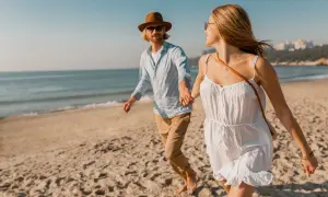Szczęśliwa para podczas spaceru nad morzem. Trzymają się za ręce, biegnąc po piaszczystej plaży.