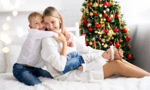 Rodzina cieszy się świętami Bożego Narodzenia w hotelu. Mama tuli synka, a córeczka śpi na jej kolanach. W tle choinka.
