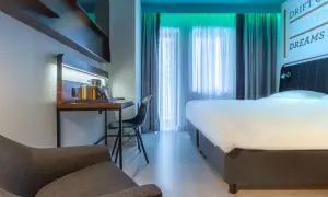 Nowoczesny pokój w Radisson Park Hotel Poznań: wygodne łóżko, biurko z czajnikiem i fotelem, zasłony i inspirujący cytat na ścianie.