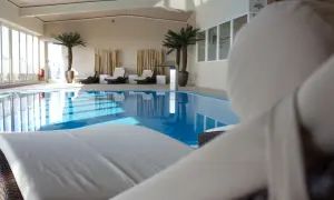 Relaks przy basenie w hotelu Radisson Blu Cottbus. Leżaki czekają na gości obok błękitnej wody i palm.