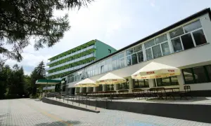 Zielony budynek sanatorium z balkonami i tarasem z parasolami Tyskie. Miejsce idealne dla szukających najlepszych sanatoriów w Polsce.
