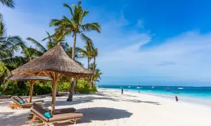 Rajska plaża z palmami i leżakami. Idealne miejsce na tani sylwester w ciepłych krajach, z turkusową wodą i łodziami na horyzoncie.