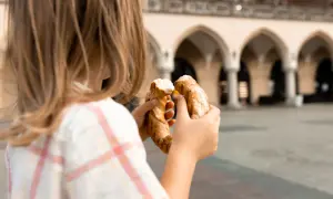 Dziecko trzyma obwarzanka na tle Sukiennic. Smaki Krakowa z dzieckiem.