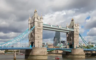 Słynny most w Wielkiej Brytanii, Tower Bridge, z charakterystycznymi wieżami i niebieskimi linami, na tle pochmurnego nieba.