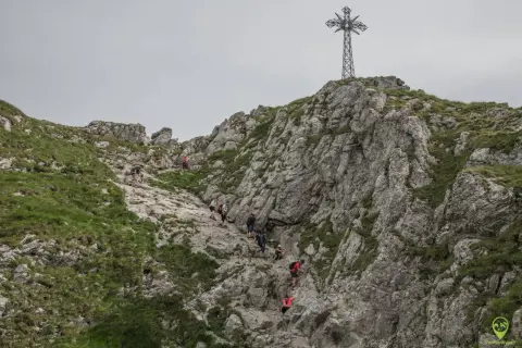 Grupa turystów wspina się po kamienistym szlaku na Giewont. W oddali widać charakterystyczny krzyż.