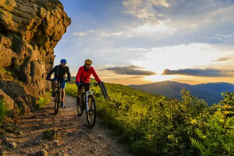 Dwóch rowerzystów przemierza malowniczą ścieżkę, odkrywając jedne z najpiękniejszych tras rowerowych w Polsce. Zachód słońca maluje niebo nad górami.