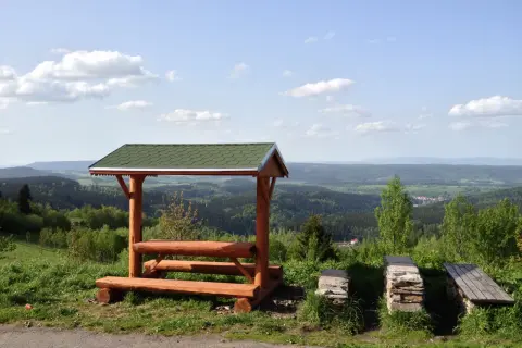 Drewniana wiata z ławkami i stołem na tle malowniczego krajobrazu Dolnego Śląska. Idealne miejsce na odpoczynek podczas zwiedzania wież widokowych.