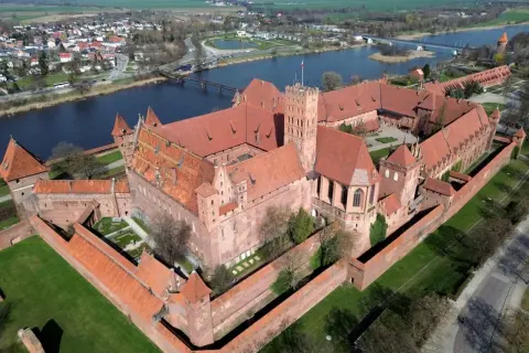 Malbork, największy zamek w Europie, rozciąga się wzdłuż rzeki. Potężne ceglane mury i czerwone dachy tworzą imponujący widok.