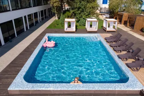 Relaks w basenie w hotelu w Karpaczu. Różowy flaming unosi się na wodzie, a obok leżaki i zaciszne altanki. Idealne miejsce na wakacje.