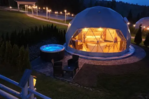 Nocny widok na hotel na szczycie góry. Dwie kopuły, jedna z wanną i łóżkiem, druga z jacuzzi na zewnątrz.