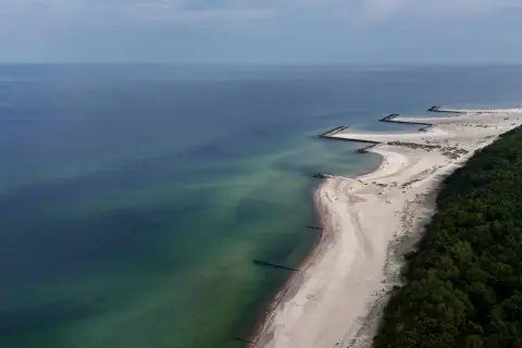 Widok z lotu ptaka na plażę w Jarosławcu z kamiennymi falochronami tworzącymi kształt przypominający molo.
