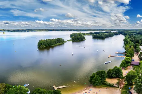 Malownicze zalewy w Polsce z żaglówkami, wyspami i plażą pełną wypoczywających ludzi.