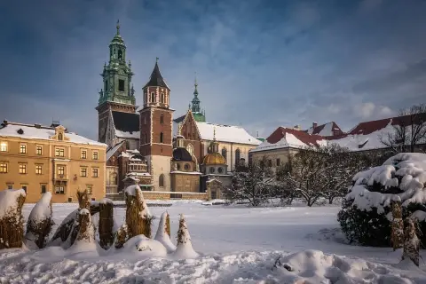 Zamek Królewski na Wawelu w zimowej scenerii. Pokryte śniegiem dachy i drzewa tworzą magiczny widok, idealny na kraków atrakcje zimą.