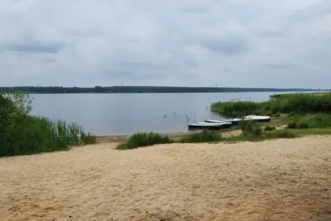 Piaszczysta plaża nad Zalewem Porajskim, z kilkoma łódkami przy brzegu. Idealne miejsce na wypoczynek i podziwianie przyrody.