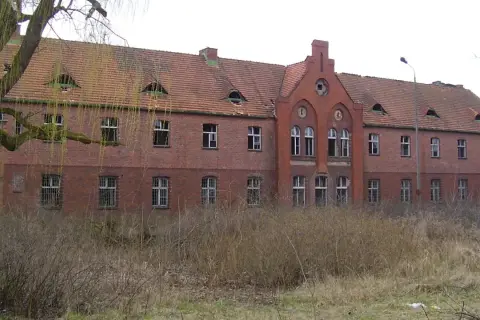 Opuszczony ceglany budynek z charakterystycznymi lukarnami i kominem. Wygląda jak jedno z tych strasznych miejsc, które kryją mroczne historie.