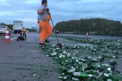 Drogi z butelkami piwa, z czym kojarzą się Niemcy. Pracownik w pomarańczowym kombinezonie sprząta autostradę.
