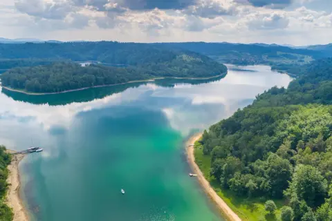 Malownicze jezioro w Polsce otoczone lasami, z łodziami przy brzegu i samotną żaglówką na wodzie. Idealne miejsce, gdzie nad jezioro w Polsce można uciec od zgiełku.