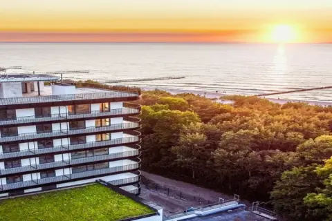 Idealny urlop nad morzem z wyżywieniem: nowoczesny hotel z widokiem na zachód słońca nad Bałtykiem, otoczony zielenią.