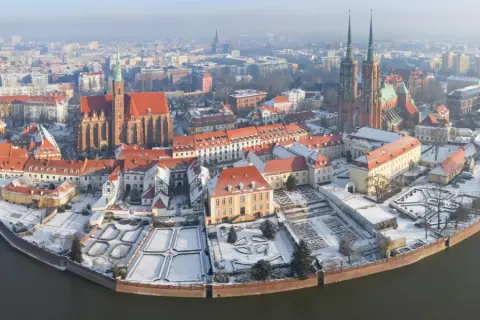 Wrocławskie atrakcje zimą: Ostrów Tumski pokryty śniegiem, z widokiem na katedrę i zabytkowe kamienice nad rzeką.