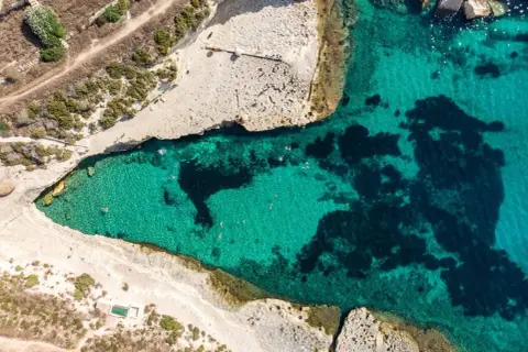 Malta plaże: turkusowa woda zatoki, skaliste wybrzeże i kilka osób kąpiących się w słońcu.