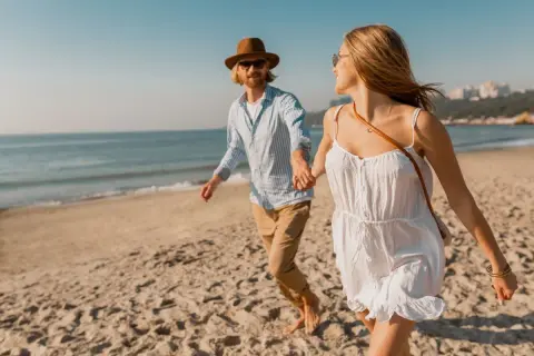 Szczęśliwa para podczas spaceru nad morzem. Trzymają się za ręce, biegnąc po piaszczystej plaży.