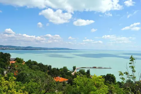 Widok na turkusowe wody Balatonu z zielonymi wzgórzami i domami. To jedno z najpiękniejszych miejsc nad Balatonem, z molo i żaglówkami na horyzoncie.