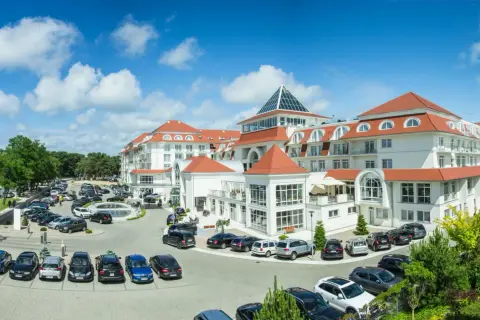 Elegancki hotel 5 gwiazdkowy nad morzem z przestronnym parkingiem pełnym samochodów.