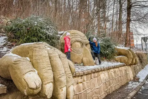 Dwie dziewczynki pozują przy gigantycznych kamiennych dłoniach i twarzy w Kudowie Zdrój. Góry w tle.