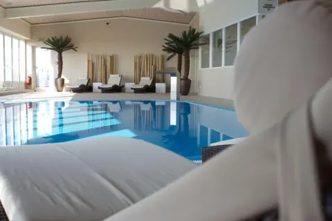 Relaks przy basenie w hotelu Radisson Blu Cottbus. Leżaki czekają na gości obok błękitnej wody i palm.