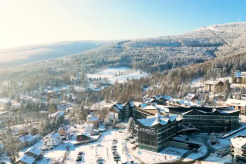 Zimowy krajobraz z hotelem Elements, który oferuje idealny hotel ze stokiem. Wokół ośnieżone drzewa i góry.