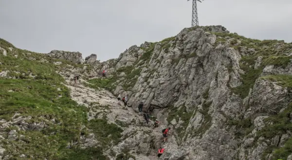 Grupa turystów wspina się po kamienistym szlaku na Giewont. W oddali widać charakterystyczny krzyż.