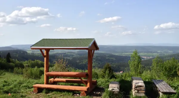 Drewniana wiata z ławkami i stołem na tle malowniczego krajobrazu Dolnego Śląska. Idealne miejsce na odpoczynek podczas zwiedzania wież widokowych.