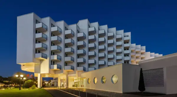 Nowoczesny hotel Amber Baltic w Międzyzdrojach o architekturze z balkonami w kształcie schodków, oświetlony wieczorem.
