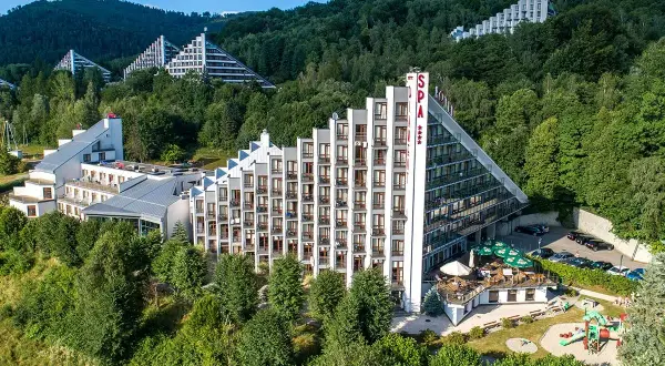 Hotel Diament Wisła w otoczeniu zieleni, z charakterystyczną architekturą schodkową i przeszklonymi fasadami.