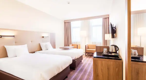 Pokój dwuosobowy w hotelu DeSilva Poznań z dwoma wygodnymi łóżkami, stolikiem i miejscem do przygotowania kawy.