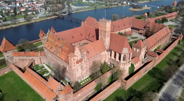 Malbork, największy zamek w Europie, rozciąga się wzdłuż rzeki. Potężne ceglane mury i czerwone dachy tworzą imponujący widok.