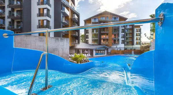 Basen z falą i zjeżdżalnią w hotelu Blue Mountain w Szklarskiej Porębie. Nowoczesne budynki hotelowe w tle.